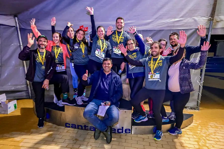Equipa com medalhas da São Silvestre 2025 no pódio, de braços no ar.